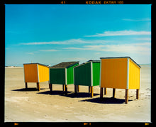 Load image into Gallery viewer, Photograph by Richard Heeps. Yellow and green beach lockers stand on their wooden legs on the clear sandy beach.
