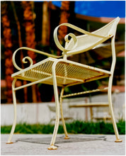 Load image into Gallery viewer, Photograph by Richard Heeps. A cream chair sits on hard standing, behind the chair and slightly out of focus is lush green grass and warm red tree trunks.