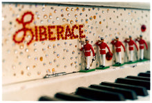 Load image into Gallery viewer, Photograph by Richard Heeps. A close up of Liberace's piano. This captures the black keys and the fall board which is decorated with crystals and red buttons spelling out Liberace in capitals. There are also 5 red and white metal soldiers positioned marching along the rim.