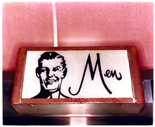 Load image into Gallery viewer, Photograph by Richard Heeps. A kitsch Men's toilet sign. The sign has the word Men alongside an outline of 1950s man. The sign sits in a wooden frame and sits against a pink tiled wall.