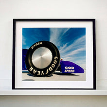 Load image into Gallery viewer, Black framed photograph by Richard Heeps. This photograph has the tyre and the very front tip of a drag car. The car's name is written on the front end "God Speed". Behind the car are white vertical clouds shooting through a blue sky.