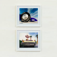 Load image into Gallery viewer, Two white framed photographs by Richard Heeps. The top photograph has the tyre and the very front tip of a drag car. The car's name is written on the front end "God Speed". Behind the car are white vertical clouds shooting through a blue sky. The bottom photo features Las Vegas and has the back of a yellow chevy car and above the car sits the sign for the Stardust casino.