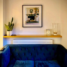 Load image into Gallery viewer, Photograph by Richard Heeps. The photograph is of a film set of 'The Outlaw Josey Wales' featuring a wooden fireplace and a black and white photo over the mantlepiece. This photograph is hung in situ in a room behind a blue sofa.