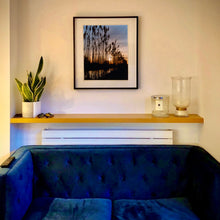 Load image into Gallery viewer, In situ black framed photograph by Richard Heeps. Reeds stand tall and reflect down onto the water with a setting sun behind them.
