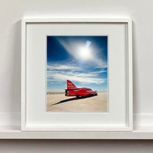 Load image into Gallery viewer, White framed photograph by Richard Heeps. A red drag car with a 75 written on its fin sits on a salt plain the front facing away towards the right. A blue cloudy sky is overhead.