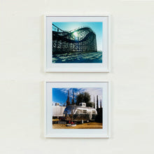 Load image into Gallery viewer, Two white framed photographs by Richard Heeps. The top photograph is the Great White Roller Coaster sitting empty on the beach in the setting sun and the photograph below is called Flamingo Trailer and depicts an aluminum airstream RV surrounded by blue sky and parched grass. In front of the trailer sits a leafless tree with two red plastic flamingos at the trees base. 