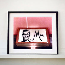Load image into Gallery viewer, A black framed photograph by Richard Heeps. A kitsch Men's toilet sign. The sign has the word Men alongside an outline of 1950s man. The sign sits in a wooden frame and sits against a pink tiled wall.