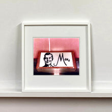 Load image into Gallery viewer, A white framed photograph by Richard Heeps. A kitsch Men's toilet sign. The sign has the word Men alongside an outline of 1950s man. The sign sits in a wooden frame and sits against a pink tiled wall.