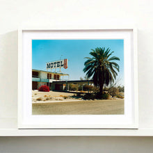 Load image into Gallery viewer, White framed photograph by Richard Heeps. A derelict motel office sits on a dusty American road. A large palm tree sits at the front of the office's walkway.