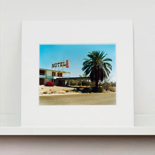 Load image into Gallery viewer, Mounted photograph by Richard Heeps. A derelict motel office sits on a dusty American road. A large palm tree sits at the front of the office's walkway.