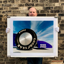 Load image into Gallery viewer, Photograph held by photographer Richard Heeps. This photograph has the tyre and the very front tip of a drag car. The car's name is written on the front end "God Speed". Behind the car are white vertical clouds shooting through a blue sky.