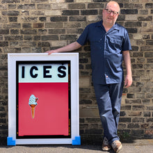 Load image into Gallery viewer, Photograph by Richard Heeps.  Richard Heeps holds a white framed print. At the top of the print, black letters spell out ICES and below is depicted a 99 icecream cone sitting left of centre against a green coloured background.  