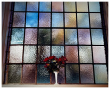 Load image into Gallery viewer, Photograph by Richard Heeps.   A small bunch of red flowers sit in a white vase in front of a coloured glass window.