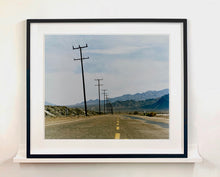 Load image into Gallery viewer, An open road in Amboy, California, featuring telephone poles disappearing into the mountainous distance. This classic and timeless landscape photograph is part of Richard Heeps' 'Dream in Colour' series. 