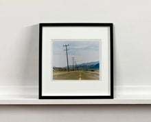 Load image into Gallery viewer, An open road in Amboy, California, featuring telephone poles disappearing into the mountainous distance. This classic and timeless landscape photograph is part of Richard Heeps' 'Dream in Colour' series. 