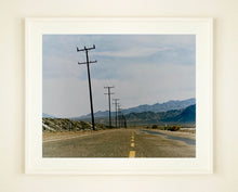 Load image into Gallery viewer, An open road in Amboy, California, featuring telephone poles disappearing into the mountainous distance. This classic and timeless landscape photograph is part of Richard Heeps' 'Dream in Colour' series. 