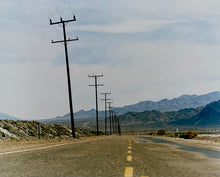Load image into Gallery viewer, An open road in Amboy, California, featuring telephone poles disappearing into the mountainous distance. This classic and timeless landscape photograph is part of Richard Heeps' 'Dream in Colour' series. 