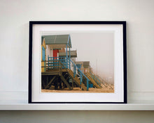 Load image into Gallery viewer, 'Beach Huts', photographed by Richard Heeps in one of his favourite areas of the UK, the port town of Wells-next-the-sea, Norfolk. This piece captures the classic quintessential beach hut on an atmospherically foggy day.