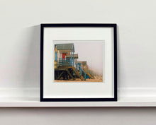 Load image into Gallery viewer, 'Beach Huts', photographed by Richard Heeps in one of his favourite areas of the UK, the port town of Wells-next-the-sea, Norfolk. This piece captures the classic quintessential beach hut on an atmospherically foggy day.