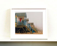 Load image into Gallery viewer, 'Beach Huts', photographed by Richard Heeps in one of his favourite areas of the UK, the port town of Wells-next-the-sea, Norfolk. This piece captures the classic quintessential beach hut on an atmospherically foggy day.