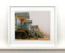 Load image into Gallery viewer, 'Beach Huts', photographed by Richard Heeps in one of his favourite areas of the UK, the port town of Wells-next-the-sea, Norfolk. This piece captures the classic quintessential beach hut on an atmospherically foggy day.