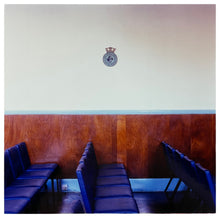 Load image into Gallery viewer, Photograph by Richard Heeps. Rows of empty blue seats facing side ways on, a Fisherman's Mission badge hangs on the white wall.