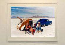 Load image into Gallery viewer, 'Christine's '52 Henry J &amp; teardrop' was captured in Bonneville Salt Flats, Utah, the iconic home of speed. This photograph shows the mountains in the distance meeting and contrasting with the flatness of the salt pan, whilst a pair of retro spectators look out at the speeding cars in the distance.