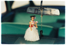 Load image into Gallery viewer, Photograph by Richard Heeps.  A hula doll sits on a dashboard, below the rear view mirror.  The car's interior is green and out of focus.