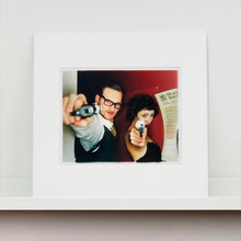 Load image into Gallery viewer, A couple look into the camera in burlesque costume against a red wall. Contemporary portrait photography by Richard Heeps mounted