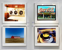 Load image into Gallery viewer, 'Stars &amp; Stripes Barn' shows a depiction of the American flag painted on this isolated building in Oakhurst, California. It sits on the horizon against a vast bright blue sky. This artwork is part of Richard Heeps' 'Dream in Colour' series.