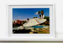 Load image into Gallery viewer, A vintage parasol, poolside at the El Morocco Motel, Las Vegas, Nevada, overlooked by palm trees, blue skies and iconic neon signs. Part of Richard Heeps' 'Dream in Colour' series.