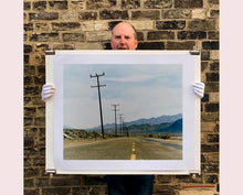 Load image into Gallery viewer, An open road in Amboy, California, featuring telephone poles disappearing into the mountainous distance. This classic and timeless landscape photograph is part of Richard Heeps' 'Dream in Colour' series. 