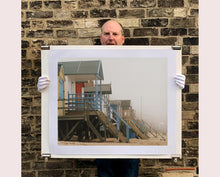 Load image into Gallery viewer, 'Beach Huts', photographed by Richard Heeps in one of his favourite areas of the UK, the port town of Wells-next-the-sea, Norfolk. This piece captures the classic quintessential beach hut on an atmospherically foggy day.
