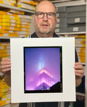 Load image into Gallery viewer, 'NOMAD VIII (Film Rebate)', New York. Richard Heeps has photographed the iconic Empire State building in the mist. The NOMAD sequence of photographs capture the art deco architecture illuminated by changing colours, and is part of Richard's street photography portfolio which depict the colour, fabric and structure of cities with distinct style. This 6x7 format edition is bordered by the Kodak film rebate. 