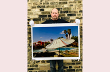 Load image into Gallery viewer, A vintage parasol, poolside at the El Morocco Motel, Las Vegas, Nevada, overlooked by palm trees, blue skies and iconic neon signs. Part of Richard Heeps' 'Dream in Colour' series.