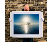 Load image into Gallery viewer, Towards Rock Hill, photographed by Richard in Bombay Beach, Salton Sea, California. The horizon intersected by sun rays, featuring a tree unexpectedly rising out of the lake gives this piece an ethereal quality. 