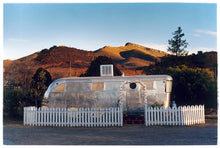 Load image into Gallery viewer, This artwork brings about a romantic dream of living in an RV. Captured in the morning sun at the start of a beautiful Arizona day, this RV is surrounded by both a white picket fence and a beautiful landscape, with the sun tickling the hilltops. Photographed as part of Richard Heeps' 'Dream in Colour' series.