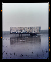 Load image into Gallery viewer, Photograph by Richard Heeps.  This photograph is tones of grey.  DEJAVU is painted on the side of a lorry trailer which sits in a grey watery fen, the sky is grey in the background. This photograph includes a film rebate.