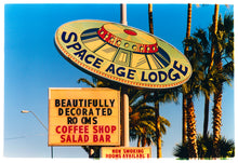 Load image into Gallery viewer, Photograph by Richard Heeps.  This retro sign takes the shape and design of a vintage UFO sign with Space Age Lodge written around the ledge of the UFO.  This is set against Arizona's palm trees and blue skies.
