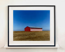Load image into Gallery viewer, 'Stars &amp; Stripes Barn' shows a depiction of the American flag painted on this isolated building in Oakhurst, California. It sits on the horizon against a vast bright blue sky. This artwork is part of Richard Heeps' 'Dream in Colour' series.