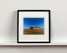 Load image into Gallery viewer, 'Stars &amp; Stripes Barn' shows a depiction of the American flag painted on this isolated building in Oakhurst, California. It sits on the horizon against a vast bright blue sky. This artwork is part of Richard Heeps' 'Dream in Colour' series.