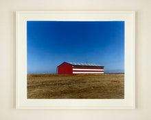 Load image into Gallery viewer, 'Stars &amp; Stripes Barn' shows a depiction of the American flag painted on this isolated building in Oakhurst, California. It sits on the horizon against a vast bright blue sky. This artwork is part of Richard Heeps' 'Dream in Colour' series.
