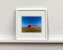 Load image into Gallery viewer, 'Stars &amp; Stripes Barn' shows a depiction of the American flag painted on this isolated building in Oakhurst, California. It sits on the horizon against a vast bright blue sky. This artwork is part of Richard Heeps' 'Dream in Colour' series.