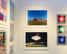 Load image into Gallery viewer, 'Stars &amp; Stripes Barn' shows a depiction of the American flag painted on this isolated building in Oakhurst, California. It sits on the horizon against a vast bright blue sky. This artwork is part of Richard Heeps' 'Dream in Colour' series.