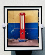 Load image into Gallery viewer, A red retro tyre pump against a yellow and blue painted wall, in the Porta Genova area of Milan. 