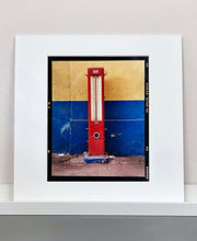 Load image into Gallery viewer, A red retro tyre pump against a yellow and blue painted wall, in the Porta Genova area of Milan. 