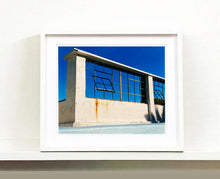 Load image into Gallery viewer, 'Window of the World, Zzyzx Resort Pool', photographed in Soda Dry Lake, California shows window pains and a distressed wall, against a bright blue background of sky. This artwork is part of Richard's 'Dream in Colour' series. 