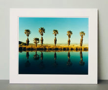 Load image into Gallery viewer, Plam trees stand tall against ombre skies in shades of blue and green in 'Zzyzx Resort Pool II', taken in Soda Dry Lake, California. This artwork was taken on a road trip from LA to Las Vegas. This photograph was taken on negative in 2002 but only executed in Richard's darkroom for the first time in 2017.